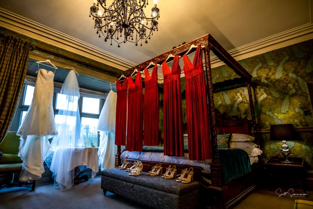 A bedroom with red dresses hanging on a four-poster bed, white wedding dresses by the window, and multiple pairs of shoes lined up at the foot of the bed. Copyright Somerside Photography Ltd // www.somersidephotography.com
