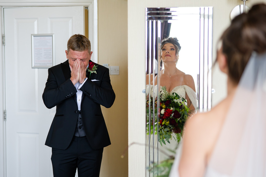 A man in a suit covers his face with his hands, while a bride holding a bouquet stands in front of him, reflected in a mirror. Copyright Somerside Photography Ltd // www.somersidephotography.com