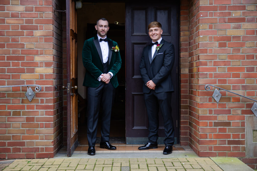 Two men dressed in formal suits stand side by side at the entrance of a brick building, posing for a photo. Copyright Somerside Photography Ltd // www.somersidephotography.com