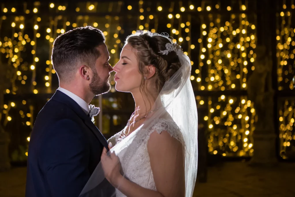 Bride and groom facing each other, about to kiss, with warm fairy lights in the background. Copyright Somerside Photography Ltd // www.somersidephotography.com