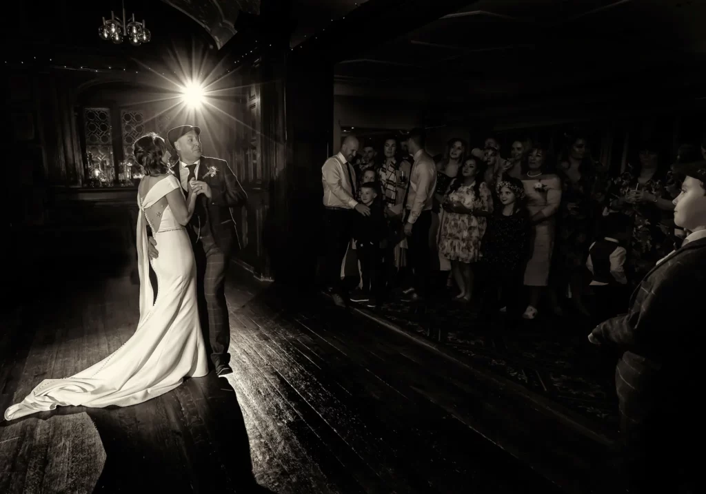 A bride and groom share a first dance on a dimly lit dance floor whilst guests watch in the background. Copyright Somerside Photography Ltd // www.somersidephotography.com