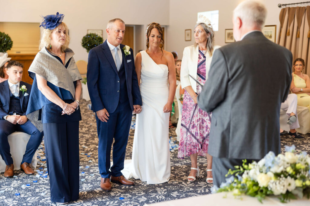A wedding ceremony with a bride and groom standing together, accompanied by two women, facing an officiant in a decorated indoor venue. Copyright Somerside Photography Ltd // www.somersidephotography.com