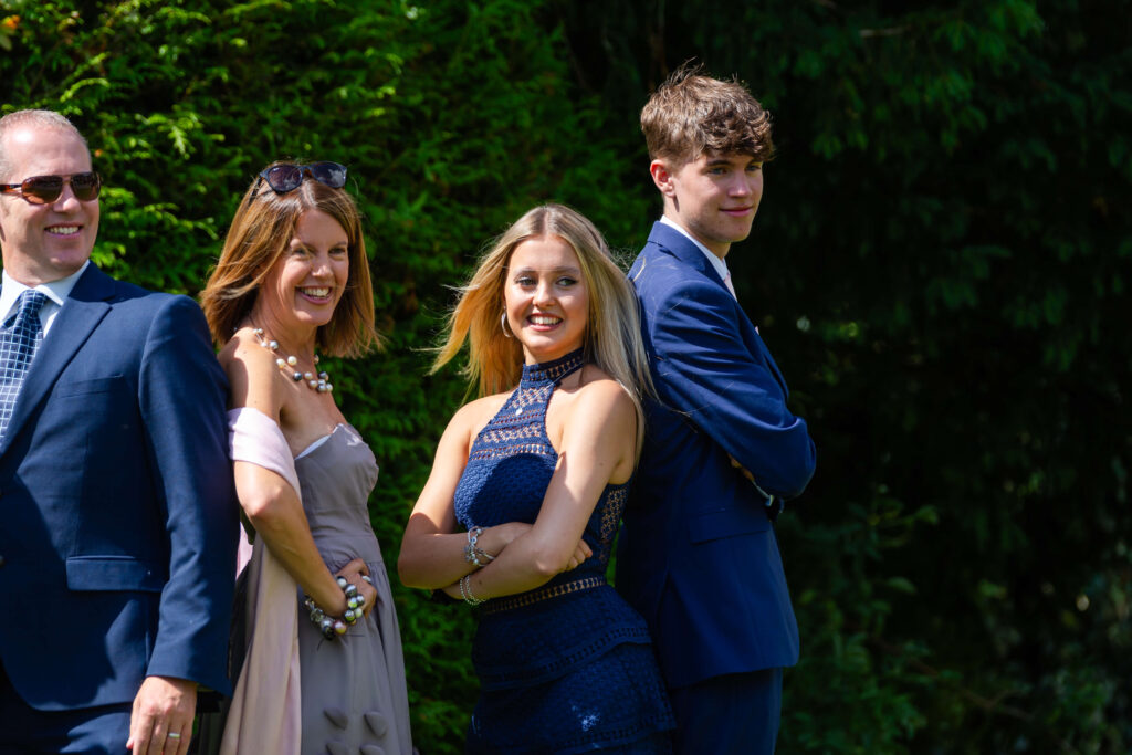 Four people wearing formal attire stand in a row outdoors, smiling or posing for a photo with greenery in the background. Copyright Somerside Photography Ltd // www.somersidephotography.com