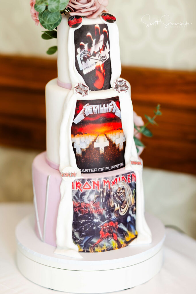 A three-tiered cake decorated with edible images of heavy metal album covers by Judas Priest, Metallica, and Iron Maiden, topped with pink roses. Copyright Somerside Photography Ltd // www.somersidephotography.com