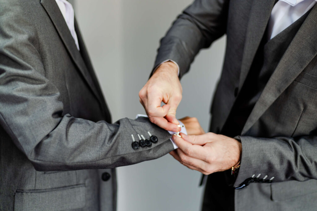 One person in a grey suit helps another person in a grey suit adjust their cufflinks. Copyright Somerside Photography Ltd // www.somersidephotography.com