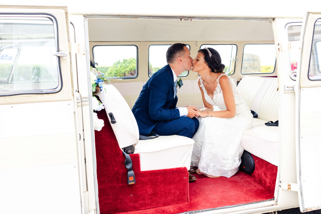 A bride and groom sit inside a white van, holding hands and sharing a kiss on their wedding day. Copyright Somerside Photography Ltd // www.somersidephotography.com
